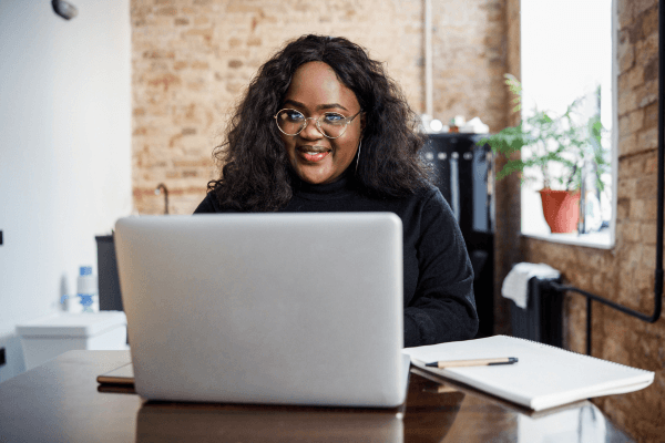 Young woman sitting at a table with a modern laptop and smiling